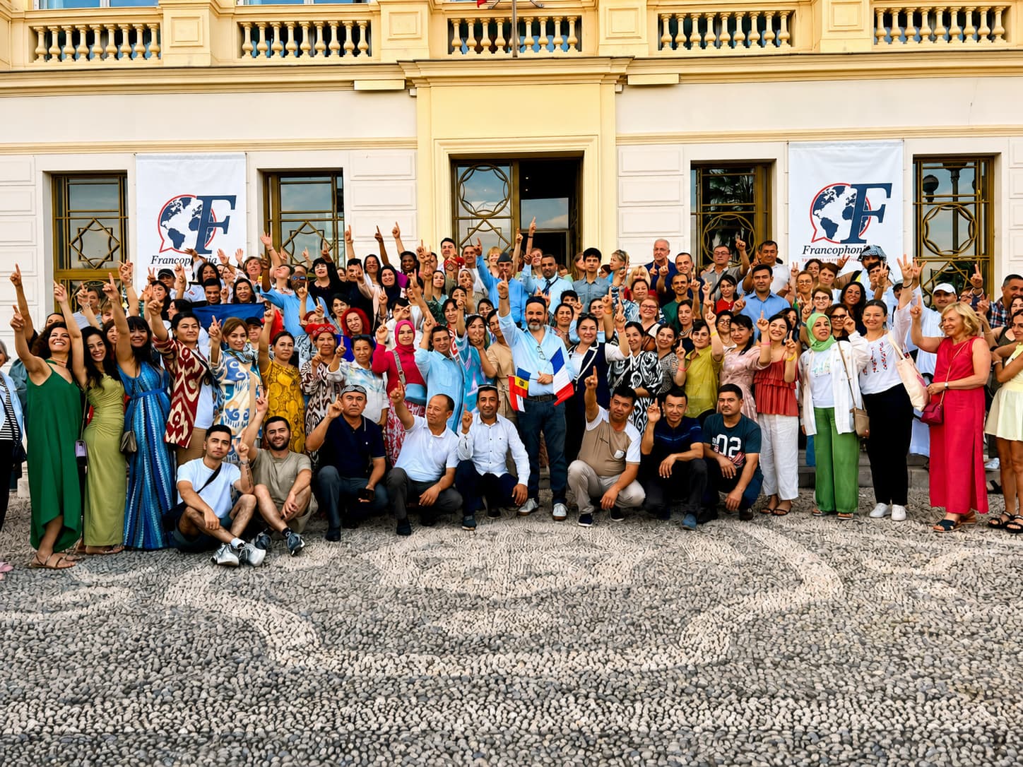 Une centaine de professeurs de nombreux pays, réunis devant une villa à Nice, la main levée vers le ciel — communauté Francophonia